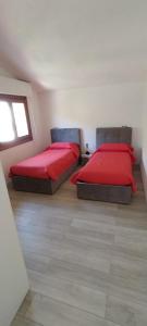 two beds in a room with red sheets and a window at Supramonte Urzulei in Urzulei