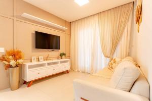 a living room with a television and a white couch at Ampla Cobertura Duplex a 120 metros da Praia de Bombas com Área de Lazer no Residencial in Bombas