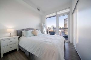 a white bedroom with a bed and a large window at RivetStays - The Jarvis in Toronto