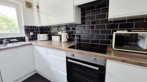 a kitchen with white cabinets and a black tile wall at Levenhowe Holiday Apartment in Balloch