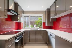 a kitchen with red walls and a sink and a window at Cosy 3 BEDROOM Home with Garden, Ealing in Greenford