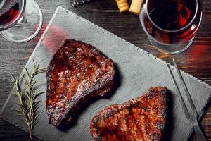 a piece of meat on a table with a glass of wine at Getaway Cottage in Drenova Glavica