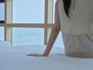 a woman sitting on a bed looking at the ocean at UH Suite The Haeundae in Busan