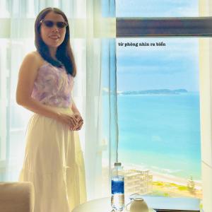 une femme en robe blanche debout devant une fenêtre dans l'établissement CONDOTEL APEC Mũi Né, à Ấp Thiẹn Ái