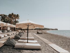 a row of white lounge chairs and umbrellas on a beach at Sagredo Boutique Hotel & Spa in Ágios Fokás