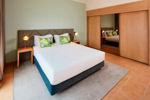 a bedroom with a large white bed and a mirror at NH Marina Portimao Resort in Portimão
