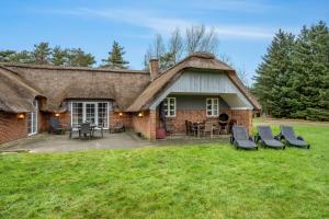 a house with a thatched roof with chairs and tables at Large Holiday Home With Pool, Spa And Sauna, 1500 Meters From The North Sea in Ulfborg