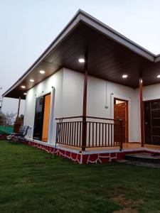 a small white house with a porch and a yard at RENI Farmstay in Karjat