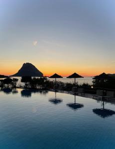 a swimming pool with umbrellas and the ocean at sunset at Hotel Don Diego in Porto San Paolo