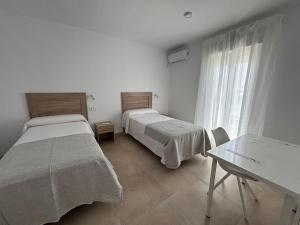 zwei Betten in einem Zimmer mit Tisch und Fenster in der Unterkunft Alojamientos VICTORIA MAR-CHIPIONA- in Chipiona