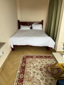 a bedroom with a bed with white sheets and a rug at Deluxe Private Studio Pad JKIA SGR in Nairobi