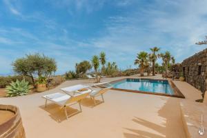 a swimming pool with two chairs next to a stone wall at Dammuso Taygeta in Pantelleria