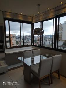 a dining room with a glass table and chairs and windows at APT Por do Sol in Bento Gonçalves