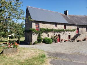 a brick building with a red door and flowers at Le Logis d'Aliénor - Baie du Mont St-Michel in Baguer-Pican
