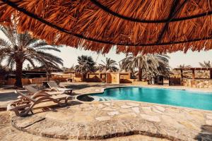 a swimming pool with chairs and a straw umbrella at Bait Ali in Wadi Rum
