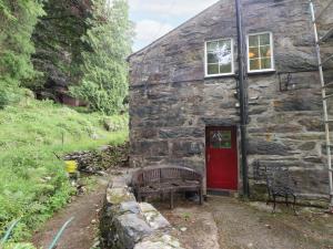 a stone house with a red door and a bench at Sygun Cottage in Caernarfon