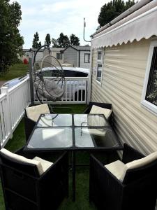 a patio with a glass table and chairs and a swing at Bright Family Caravan with Deck & BBQ at Seawick Holiday Park, Clacton in Clacton-on-Sea