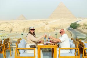 un hombre y una mujer sentados en una mesa frente a las pirámides en Hayat Pyramids View Hotel, en El Cairo