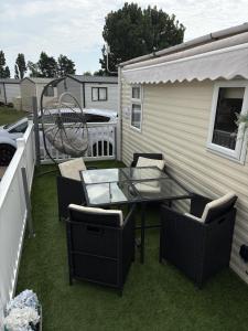 a patio with a glass table and chairs on the grass at Bright Family Caravan with Deck & BBQ at Seawick Holiday Park, Clacton in Clacton-on-Sea