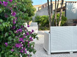 Dos sillas de mimbre blancas junto a un arbusto con flores moradas. en L'araucaria Le Camere, en Riola Sardo