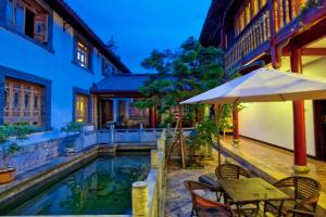 an umbrella and tables and chairs next to a swimming pool at Lijiang Wangfu Hotel in Lijiang