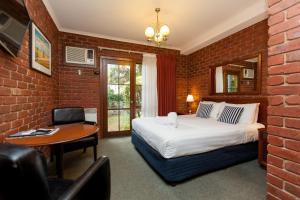 a bedroom with a bed and a desk and a brick wall at Armour Motor Inn in Beechworth