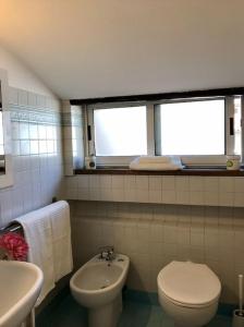 een badkamer met een toilet, een wastafel en 2 ramen bij Mansarda la Graziosa in Rimini