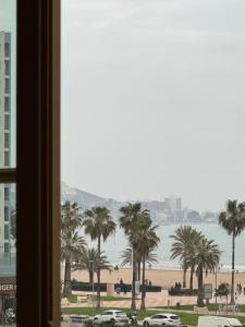 een raam met uitzicht op het strand en palmbomen bij Wagner Playa Apartment in Cullera
