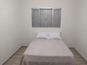 a bed in a white room with a window at Casa para Temporada in São Thomé das Letras