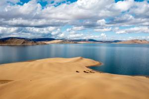 a lake in the desert with a sand dune next to the water at Tosontsengel Glamping Tents 