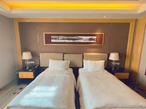 two beds in a hotel room with two lamps at Wanda Realm Dandong in Dandong