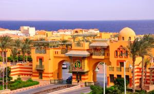 a yellow building with palm trees in front of the ocean at Rehana Royal Beach Resort - Aquapark & Spa - Family & Couples Only in Sharm El Sheikh