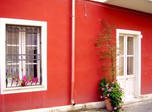 a red building with two windows and flowers on it at S'Attobiu Guest Rooms in Teulada