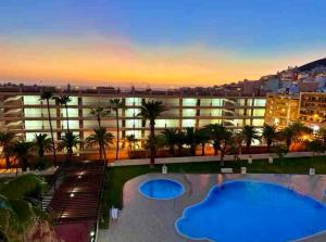 a building with two swimming pools and palm trees at Seaside Two Bedroom Apartment in Los Cristianos