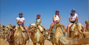 three people riding on the backs of camels in the desert at Riad dar asalam in Agadir