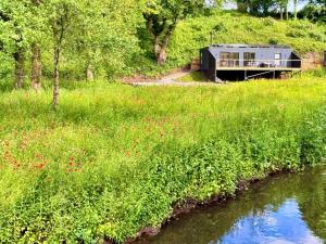 a house on a hill next to a river at Kingfisher - Luxurious Off-Grid Eco Cabin with Riverviews in Market Drayton