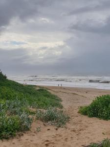 a beach with people walking on the sand and the ocean at Deep Blue Guest House in Amanzimtoti