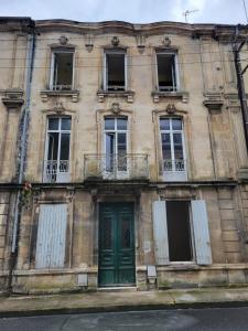 an old building with a green door and windows at Le Duplex Bordeaux in Saint-Jean-dʼAngély