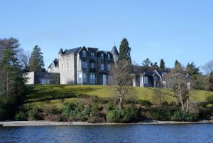 a large building on a hill next to a body of water at No 8 Lomond Castle in Luss
