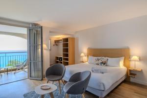 a bedroom with a bed and chairs and a balcony at Hôtel La Villa Douce in Rayol-Canadel-sur-Mer