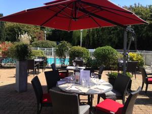a table with a red umbrella on a patio at Mercure Paris Le Bourget Aeroport in Le Blanc-Mesnil