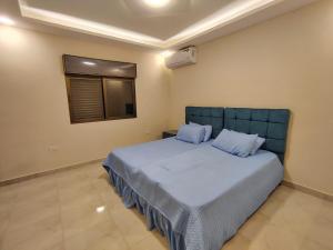 a bedroom with a bed with blue sheets and a window at Janna2Villa in Tall al Misţāḩ