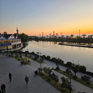 Orbi city mia luxury studio في باتومي: منظر لنهر عند غروب الشمس مع أشخاص يتجولون حوله