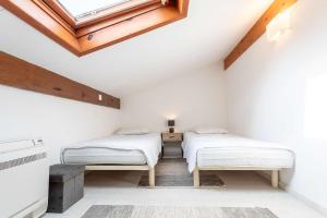 two beds in a white room with a skylight at Proche lac : Maison avec beau jardin in Biscarrosse