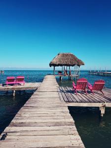 un muelle con sillas y una sombrilla de paja en el agua en Barefoot Beach Belize, en Caye Caulker