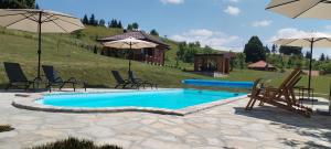 a swimming pool with chairs and umbrellas and a house at Turizam Koturovic in Ivanjica