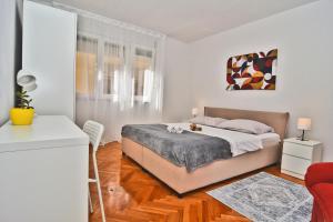 a white bedroom with a bed and a red chair at Apartman Mario in Zadar