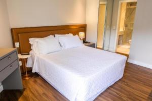 een slaapkamer met een wit bed met een houten hoofdeinde bij Apto Studio Hotel Praia Brava in Florianópolis +15 foto's