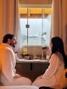 a man and a woman sitting at a table with drinks at Chalés Vila do Moinho in Monte Verde +40 photos