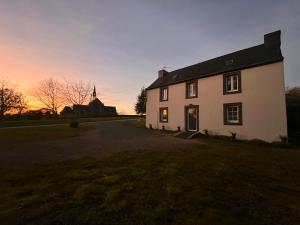 una casa bianca con una chiesa sullo sfondo di Ti ar Goanag, Maison de vacances, Séjour, Week-end a Pleyben